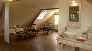 A room with a sloped ceiling, a dining area with wooden furniture, a white sink with a mirror, and a window with a view. - Loargann Chambres d'Hotes (Plogastel-Saint-Germain)