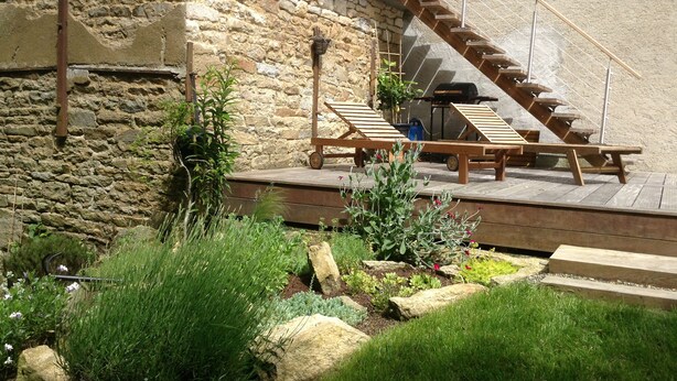 A wooden deck with lounge chairs, a barbecue grill, and a stone wall. - Loargann Chambres d'Hotes (Plogastel-Saint-Germain)
