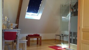 A room with a skylight, a wooden floor, a small table with a red cloth, a chair, and a glass shower enclosure. - Loargann Chambres d'Hotes (Plogastel-Saint-Germain)
