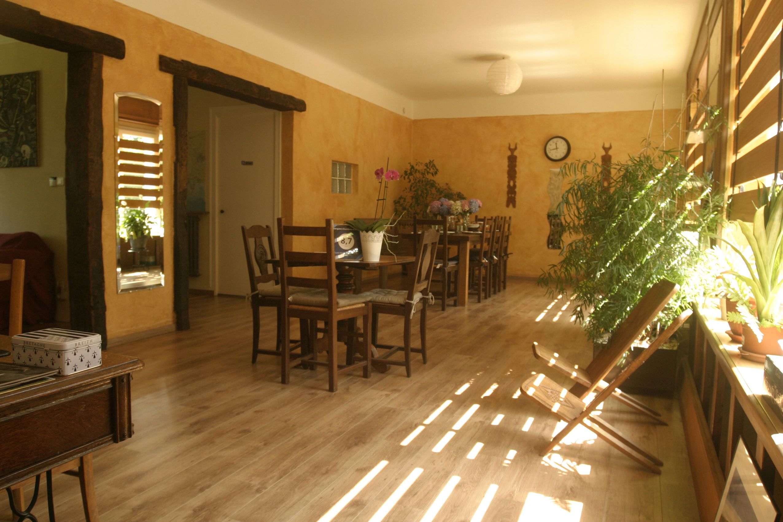 A dining area with wooden furniture, a clock on the wall, and potted plants.