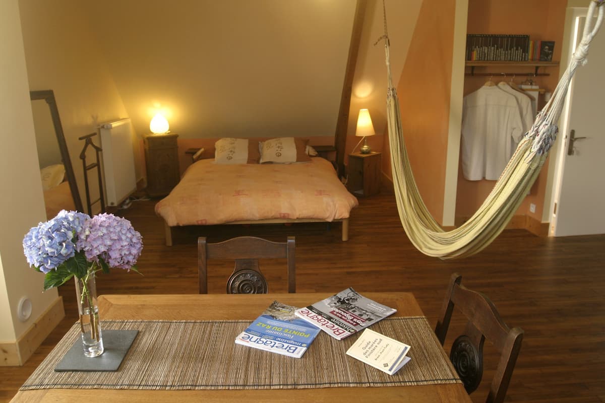 Ein Schlafzimmer mit Bett, Nachttischlampen, einer Hängematte, einem Tisch mit Büchern und einer Blumenvase.