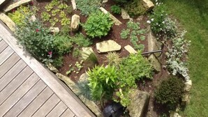 A garden bed with various plants and rocks, bordered by a wooden deck. - Loargann Chambres d'Hotes (Plogastel-Saint-Germain)