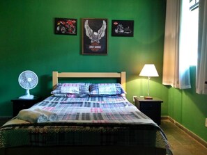 A bedroom with a bed, a fan, a lamp, and three framed pictures on the wall. - Road House GO 118 Motorcycle Hotel (Alto Paraíso de Goiás)
