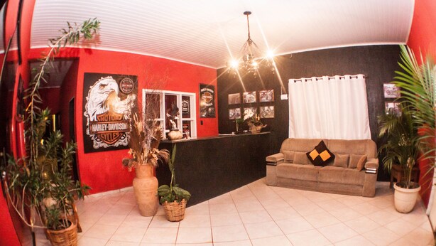 A room with a red wall, a black counter, a beige sofa, and potted plants. - Road House GO 118 Motorcycle Hotel (Alto Paraíso de Goiás)