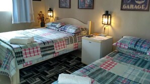A hotel room with two beds, each with a plaid bedspread and a white towel on the bed. There are wall-mounted air conditioning units and framed posters on the walls. - Road House GO 118 Motorcycle Hotel (Alto Paraíso de Goiás)