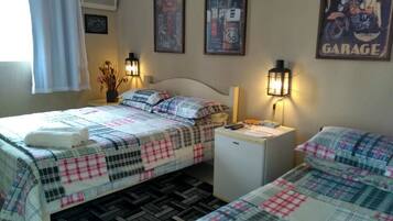 Quarto de hotel com duas camas, cada uma com colcha xadrez e toalha branca. Há unidades de ar condicionado montadas na parede e cartazes emoldurados.