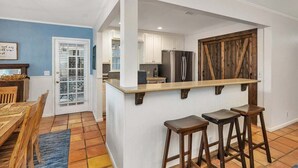 Eine Küche mit Kochinsel, Barhocker, Kühlschrank und einer Staldtür.