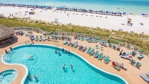 Uma área de piscina com várias pistas de natação e espreguiçadeiras, rodeada por uma praia de areia e uma vista deslumbrante do oceano.