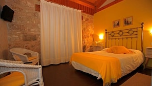 Un dormitorio acogedor con una cama, dos sillas de mimbre, un muro de piedra y un techo de madera.