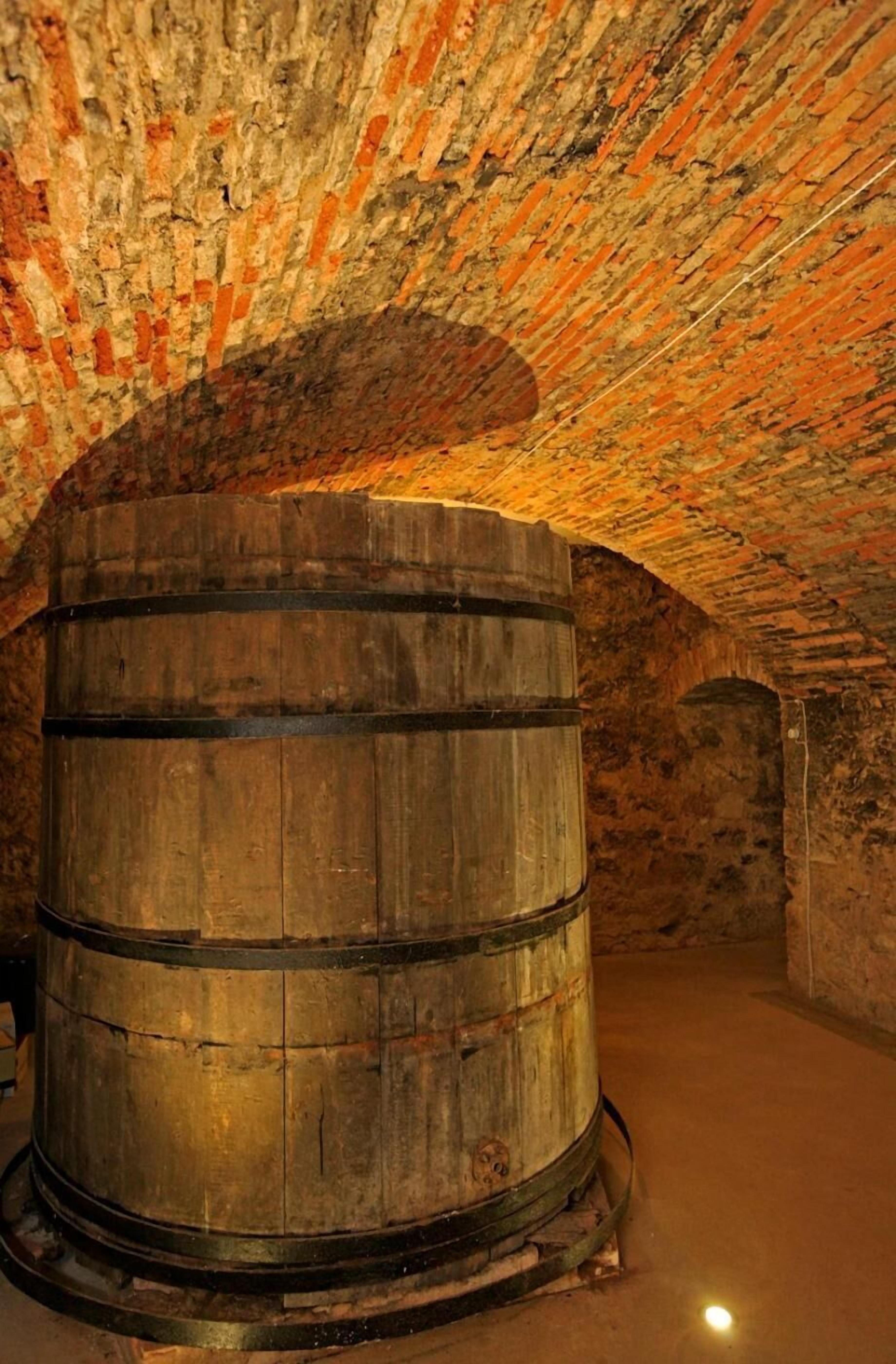 Un barril de madera grande en una habitación poco iluminada con paredes de ladrillo en arco.