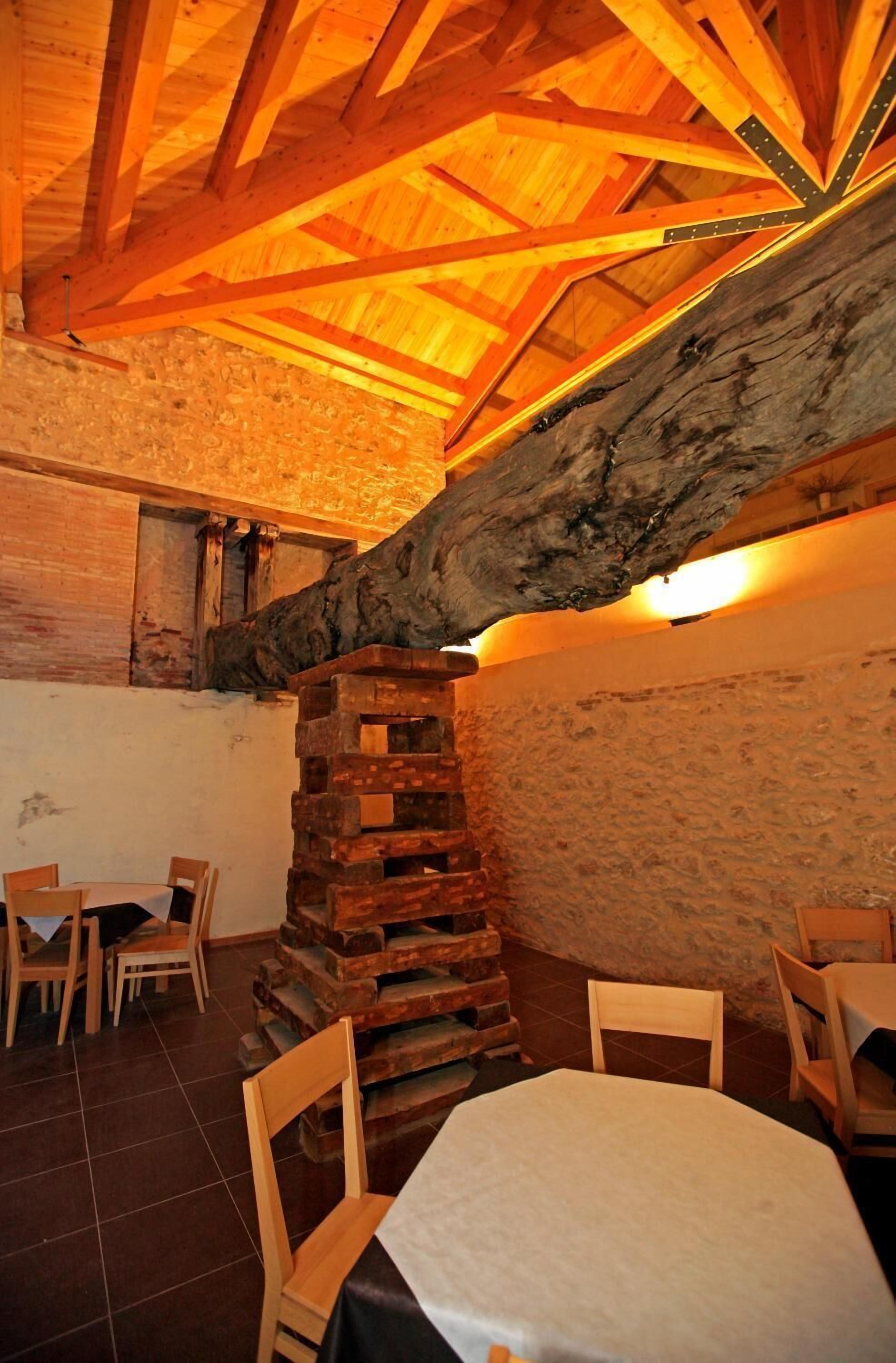A rustic interior with exposed wooden beams, a stone wall, and a wooden staircase.