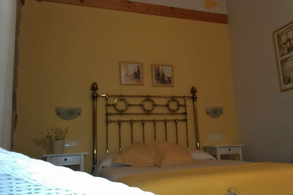 Un dormitorio con cama, mesita de noche, lámpara y dos cuadros en la pared.