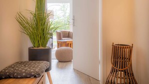 Un couloir avec une plante en pot, une chaise en osier et un pouf rond.