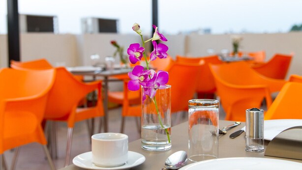 A dining table with a white cup, a glass of water, and a vase with purple flowers.