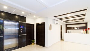 A hotel reception area with a reception desk, a digital screen, and an elevator.