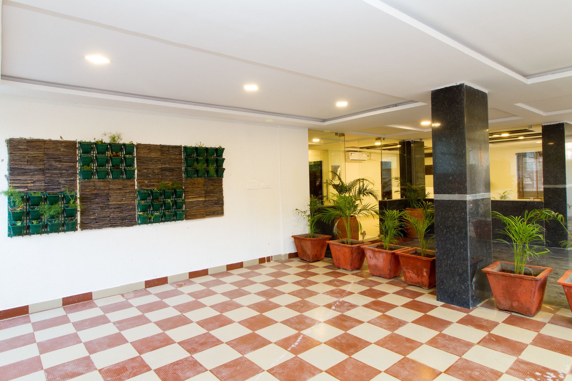 Un vestíbulo con piso a cuadros, macetas verdes y un jardín vertical en la pared.