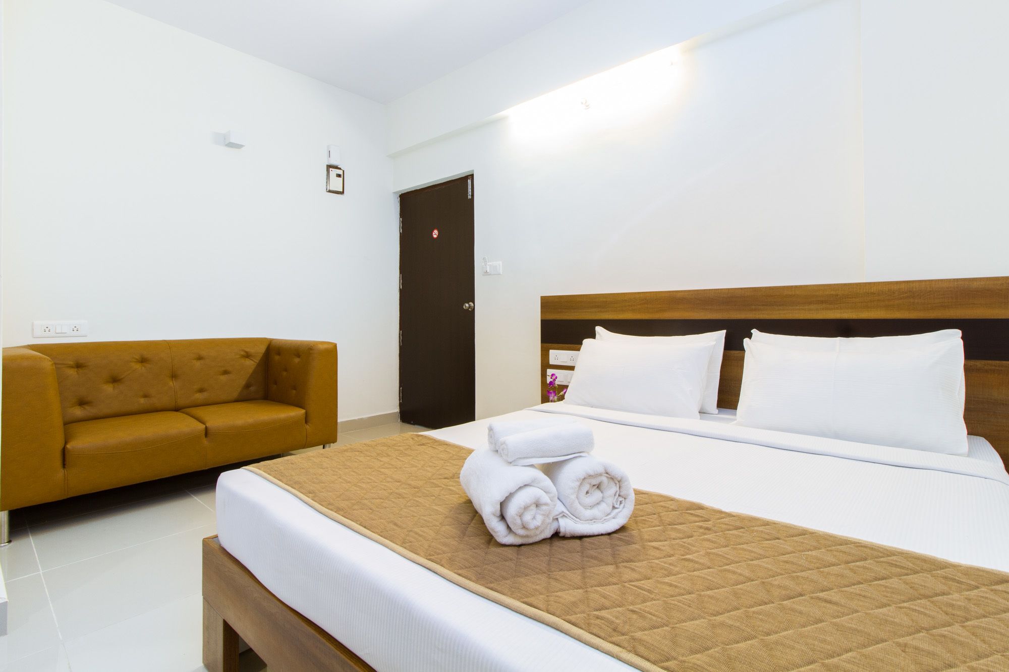 Una camera d'albergo con un letto, un divano marrone e una porta.