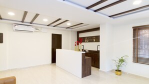 A hotel reception area with a modern design, featuring a reception desk, a large window with blinds, and a ceiling with exposed beams.
