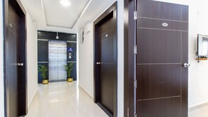 A hallway with two dark wooden doors, a marble floor, and a glass elevator door.