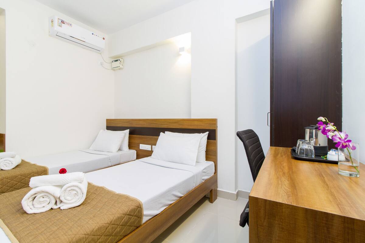 Ein Hotelzimmer mit zwei Einzelbetten, einem Holzkopfende, einem Schreibtisch mit Stuhl und einem kleinen Tisch mit Blumen.