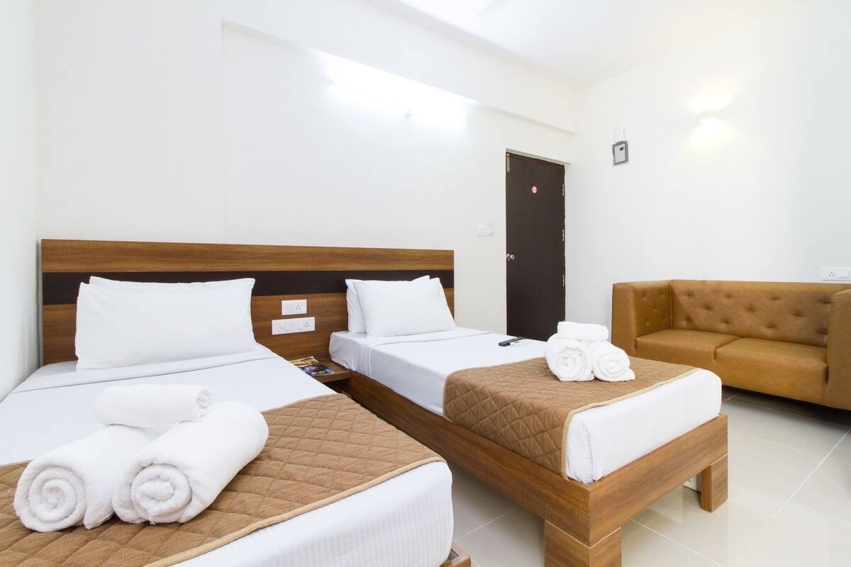 Ein Hotelzimmer mit zwei Betten, einem braunen Sofa und einer Tür.