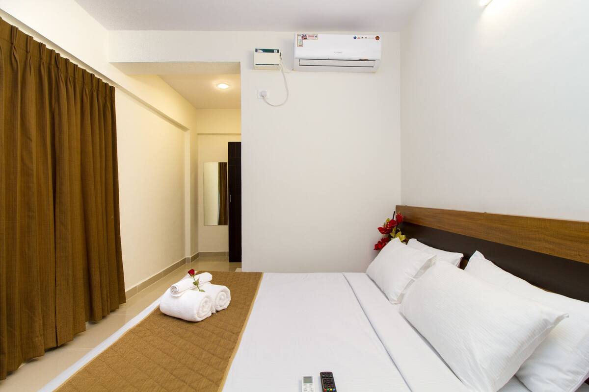 Ein Hotelzimmer mit einem Bett, einer Fernbedienung, einem Handtuch mit Rosenmotiv und einer Klimaanlage.