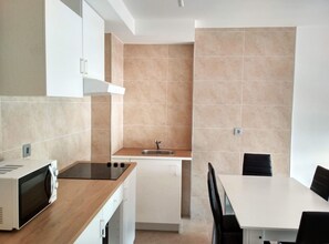 Cocina compacta con microondas, estufa, pileta y alacenas blancas. Hay una mesa de comedor con sillas.