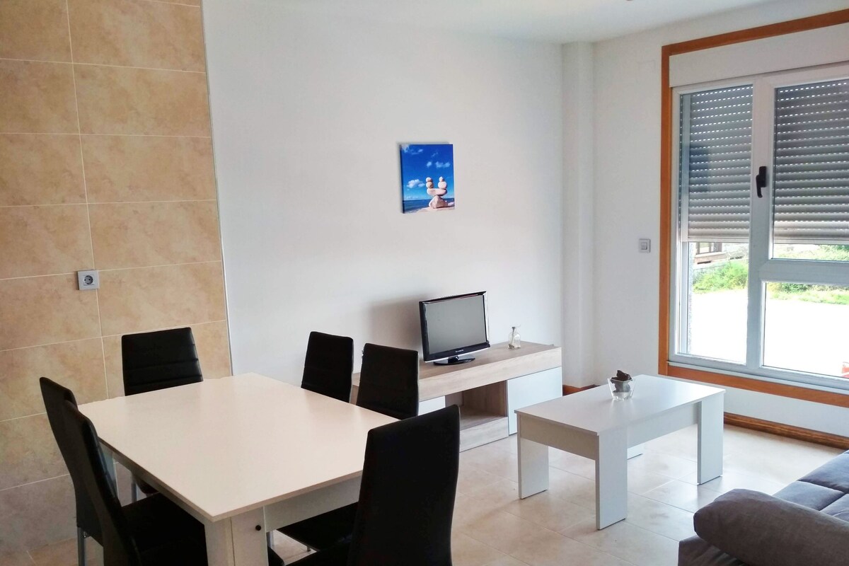 Una sala de estar moderna con comedor, televisor de pantalla plana y un amplio ventanal con persianas.