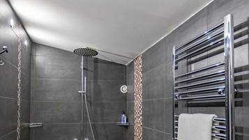 A modern shower with a handheld showerhead, a built-in soap dispenser, and a towel rack with two towels.