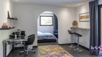 Un dormitorio moderno con cama, escritorio, silla y un pequeño rincón de descanso con dos taburetes.