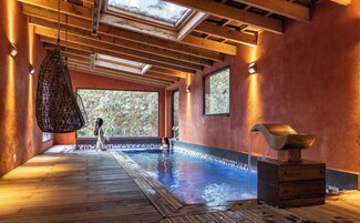 Un área de spa con terraza de madera, piscina y un amplio ventanal con vistas a árboles.