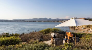 Une vue sur la côte, avec une plage, des chaises longues et un grand parasol qui offre de l’ombre.