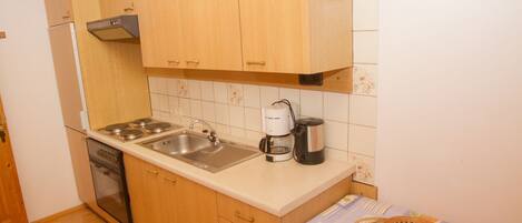 Una cocina compacta con armarios de madera, horno integrado, pileta y cafetera.