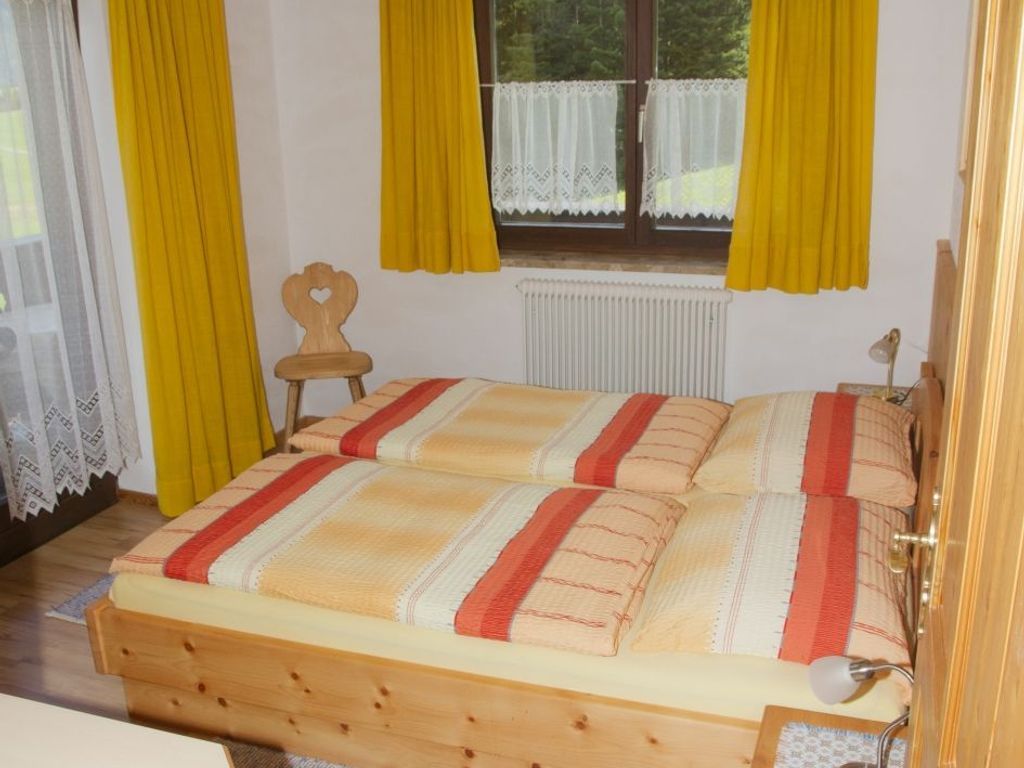 Ein Zimmer mit einem hölzernen Bett, gelben Vorhängen, einer Heizung und einem Fenster mit Spitzendeckchen.