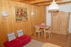 A wooden interior with a red sofa, a dining table with chairs, a painting of flowers, and a large cabinet. - Apartment Römerweg - House Römerweg (Strobl)