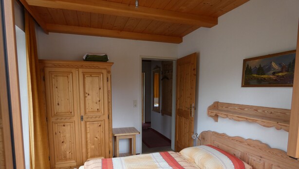 A bedroom with a wooden bed, a wardrobe, a small bedside table, and a painting on the wall.