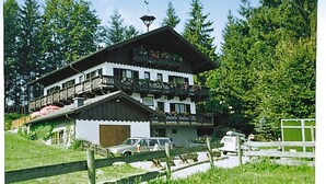 A multi-story building with balconies, a car parked in front, and a wooden fence.