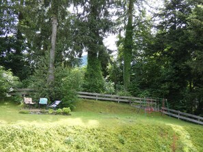 A wooded area with a wooden fence, a swing set, and a bench. - Apartment Römerweg - House Römerweg (Strobl)
