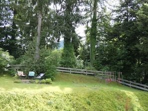 A wooded area with a wooden fence, a swing set, and a bench.