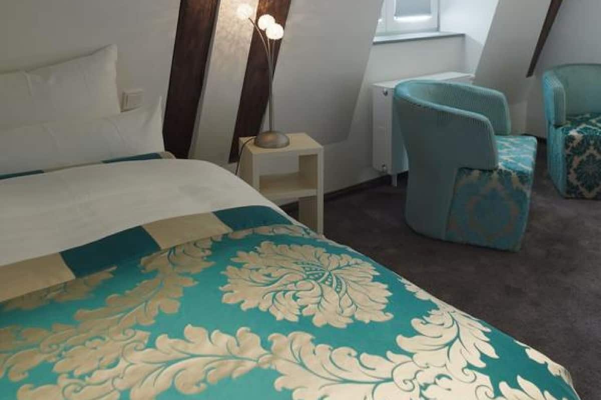 A bedroom with a bed, a nightstand, a lamp, and two chairs.