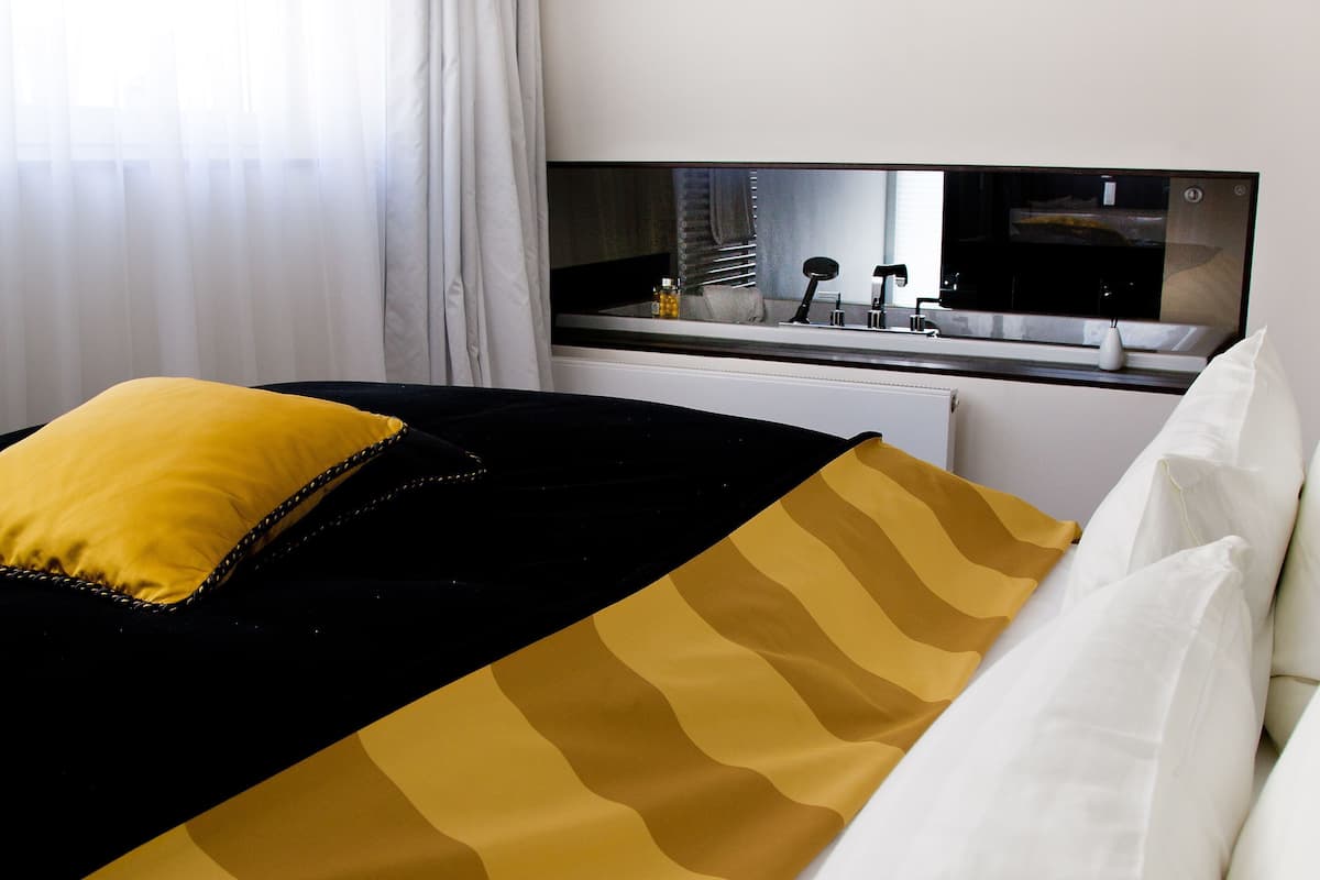 A hotel room with a bed, a bedside table, a mirror, and a window with curtains.