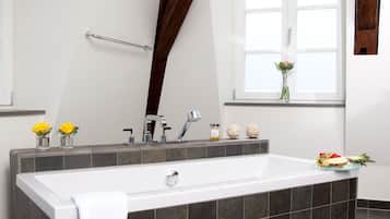 Une salle de bain moderne avec une grande baignoire, un carrelage foncé, une fenêtre offrant une belle vue et une poutre en bois au plafond.
