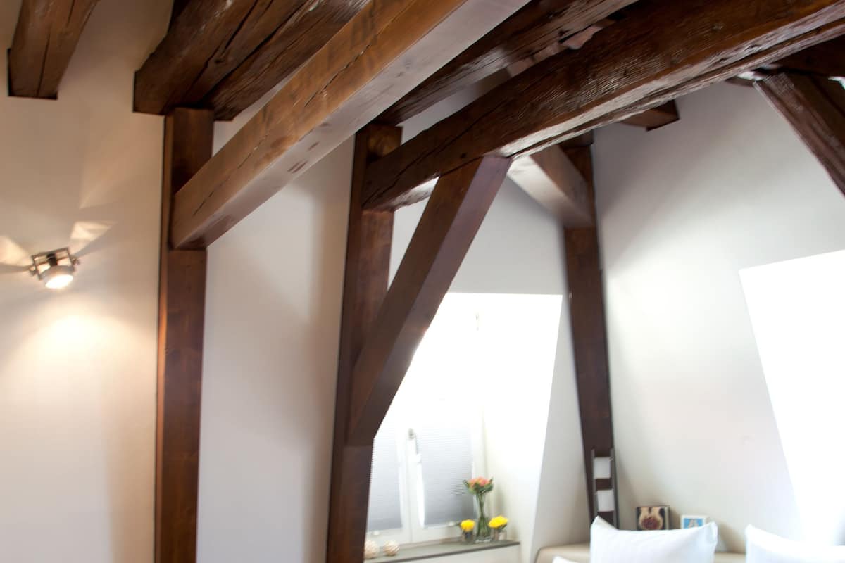 A bedroom with a large bed, wooden beams, a bedside table, and a nightstand.