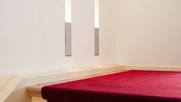 Esquina de una habitación con piso cubierto de alfombra roja y una pared blanca con dos lámparas verticales.