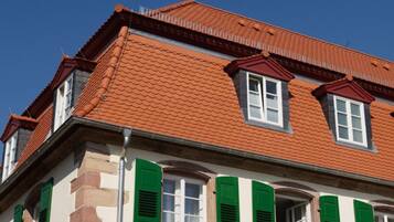Un bâtiment avec un toit recouvert de tuiles rouges, des volets verts et une façade en pierre.