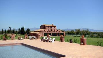 A large building with a swimming pool, outdoor seating, and a well-maintained lawn.