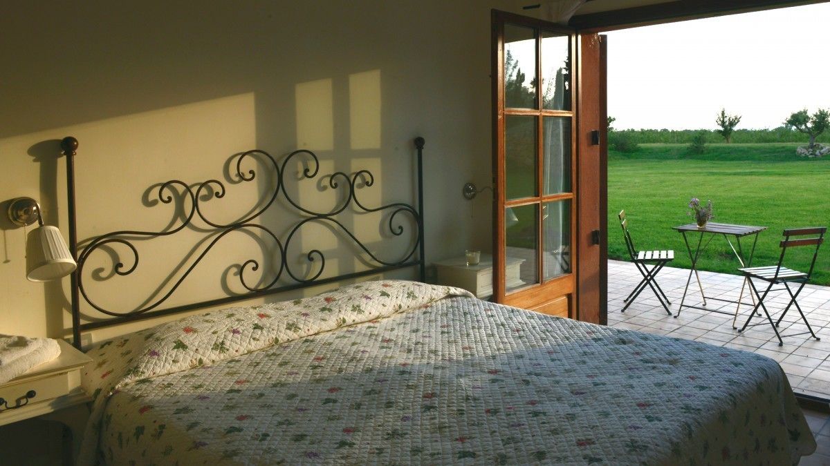 A bedroom with a bed, a bedside table, a lamp, and a view of a patio with a table and chairs.