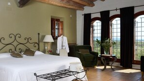 Ein Schlafzimmer mit Bett, Stuhl, Tisch und einem Fenster mit Vorhängen.