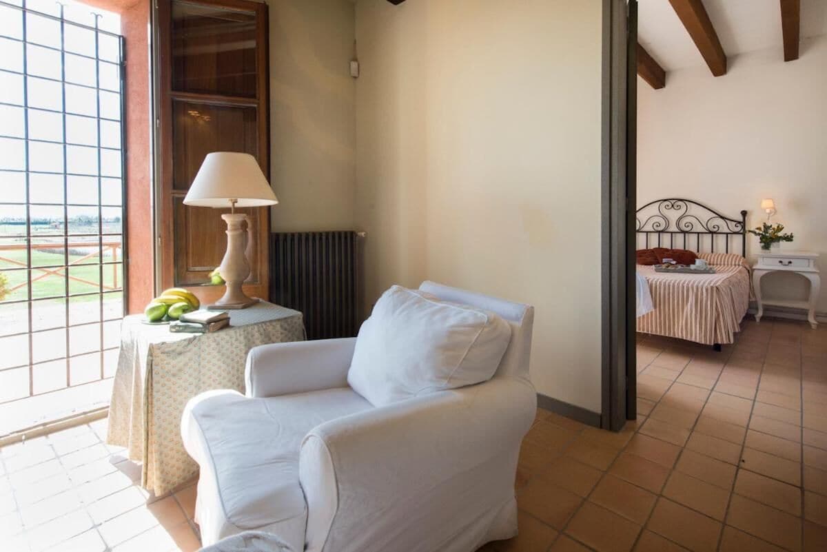 Una habitación con un sillón blanco, una mesa con lámpara y una cama con ropa de cama a rayas.