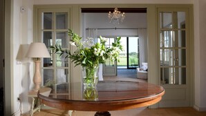 A room with a round table, a vase with flowers, a lamp, and a view of the outdoors through a door. - Mas del Mar (Sant Pere Pescador)